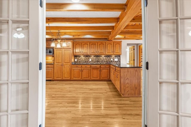 kitchen with stainless steel microwave, decorative backsplash, beam ceiling, and light hardwood / wood-style flooring