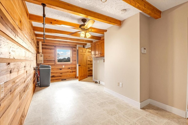 spare room featuring ceiling fan, wooden walls, beamed ceiling, and a textured ceiling