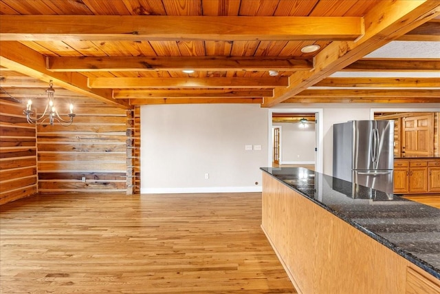 kitchen featuring stainless steel refrigerator, decorative light fixtures, light wood-type flooring, dark stone counters, and beam ceiling