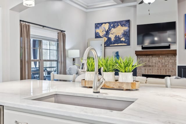 details featuring sink, ceiling fan, light stone counters, crown molding, and a brick fireplace