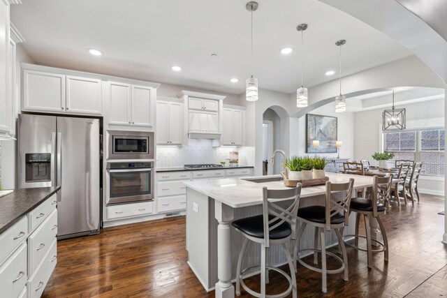 kitchen with pendant lighting, sink, white cabinets, stainless steel appliances, and a center island with sink