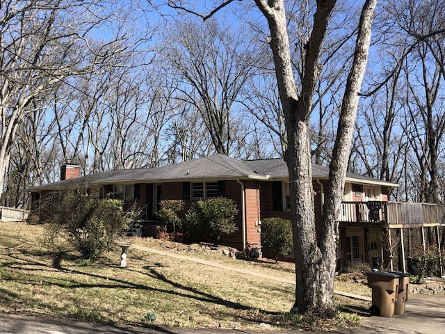 ranch-style home with driveway, a chimney, a wooden deck, a front lawn, and brick siding