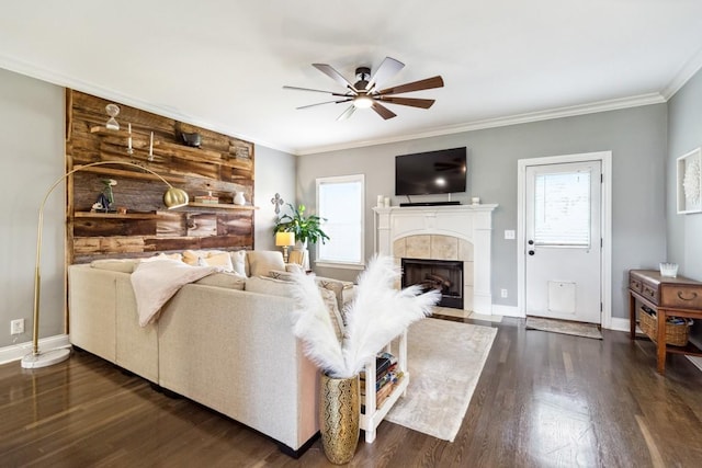 living room with a tiled fireplace, crown molding, dark wood-type flooring, and ceiling fan