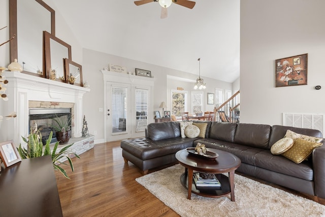 living room with vaulted ceiling, a stone fireplace, ceiling fan with notable chandelier, and hardwood / wood-style floors