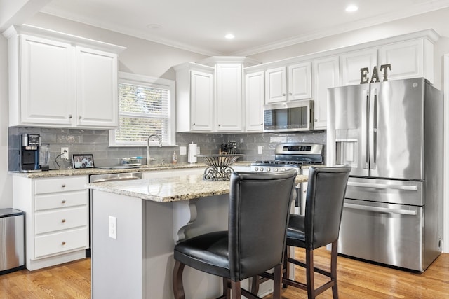 kitchen featuring appliances with stainless steel finishes, a breakfast bar area, white cabinets, decorative backsplash, and a center island