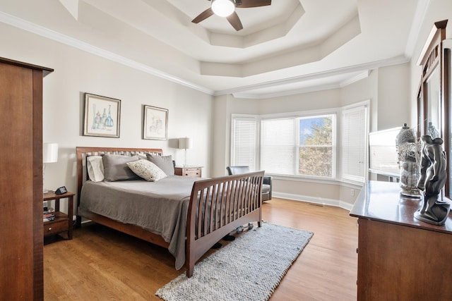 bedroom with crown molding, a raised ceiling, ceiling fan, and light wood-type flooring