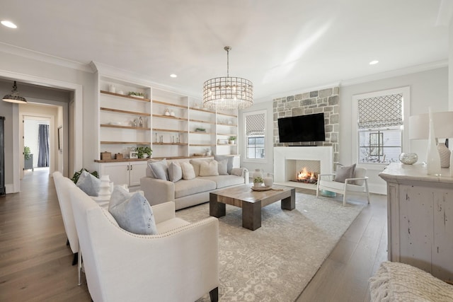 living room featuring an inviting chandelier, a stone fireplace, ornamental molding, and light hardwood / wood-style floors