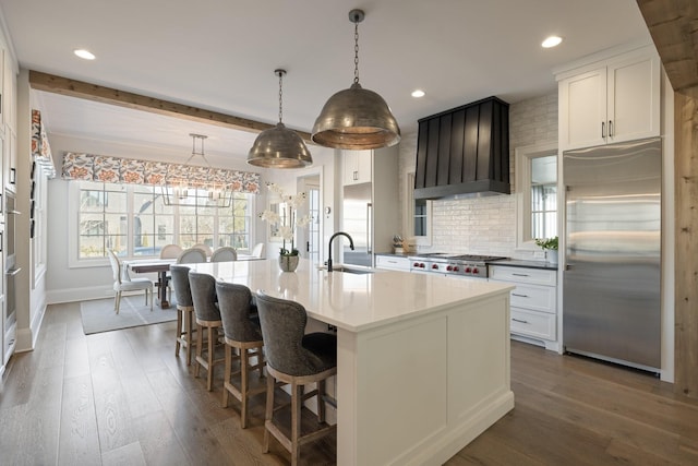 kitchen featuring white cabinetry, stainless steel appliances, an island with sink, and beamed ceiling