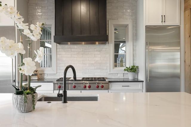 kitchen featuring custom exhaust hood, built in refrigerator, light stone countertops, and decorative backsplash