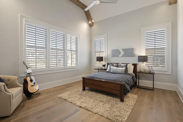 bedroom with ceiling fan, hardwood / wood-style floors, multiple windows, and vaulted ceiling with beams