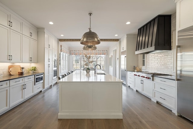 kitchen with appliances with stainless steel finishes, decorative light fixtures, white cabinetry, sink, and a kitchen island with sink