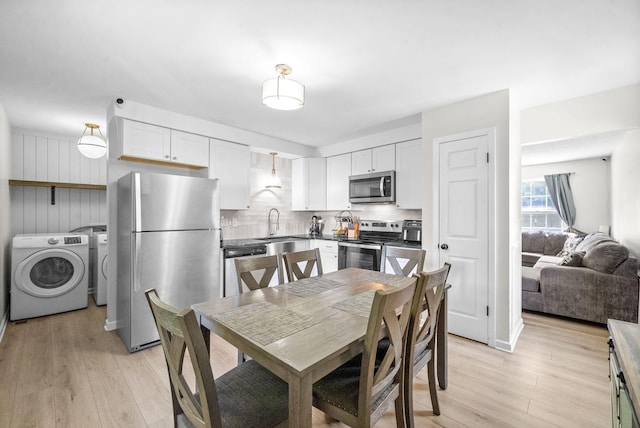 kitchen featuring white cabinets, appliances with stainless steel finishes, pendant lighting, and washing machine and clothes dryer