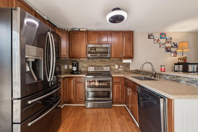 kitchen with sink, light wood-type flooring, appliances with stainless steel finishes, kitchen peninsula, and decorative backsplash