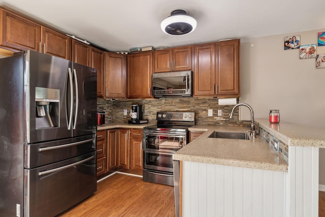 kitchen featuring sink, light hardwood / wood-style flooring, appliances with stainless steel finishes, kitchen peninsula, and decorative backsplash