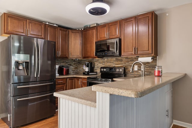 kitchen with decorative backsplash, light hardwood / wood-style flooring, kitchen peninsula, and appliances with stainless steel finishes