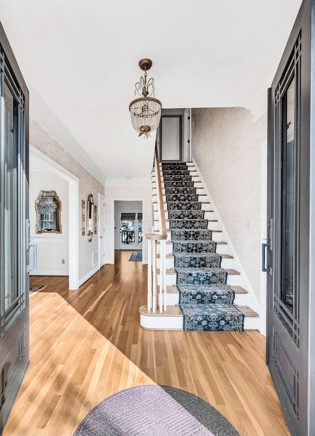 foyer entrance featuring an inviting chandelier, wood-type flooring, and ornamental molding