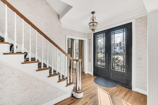 foyer entrance with hardwood / wood-style floors, crown molding, french doors, and a chandelier