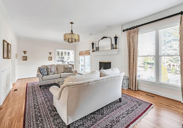 living room featuring a brick fireplace, plenty of natural light, ornamental molding, and light wood-type flooring