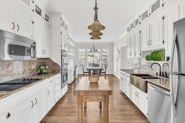 kitchen featuring white cabinetry, ornamental molding, pendant lighting, stainless steel appliances, and light stone countertops