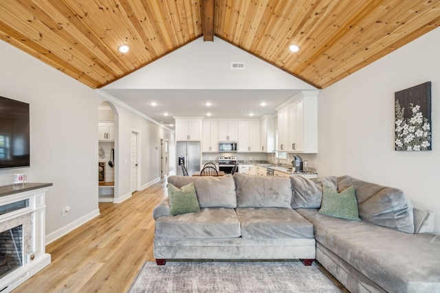 living room featuring sink, wood ceiling, lofted ceiling with beams, light hardwood / wood-style floors, and a stone fireplace