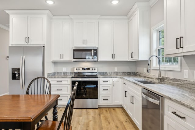 kitchen featuring stainless steel appliances, white cabinetry, sink, and light stone counters