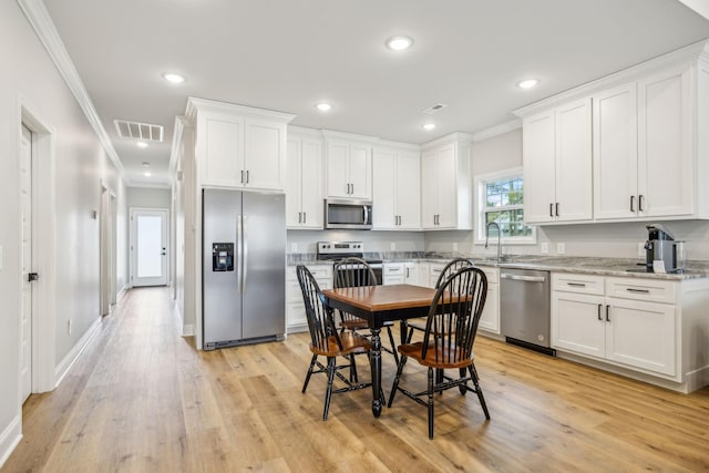 kitchen with light stone countertops, white cabinetry, appliances with stainless steel finishes, and light wood-type flooring