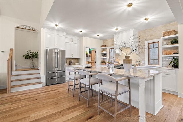 kitchen with white cabinetry, a kitchen island with sink, light stone counters, high quality fridge, and light hardwood / wood-style floors