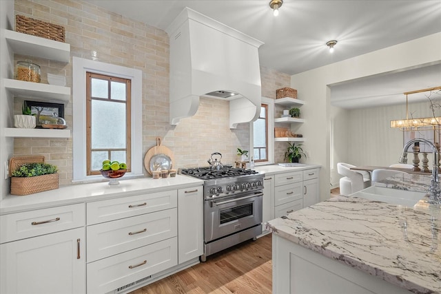 kitchen with sink, light hardwood / wood-style flooring, white cabinetry, high end stove, and custom exhaust hood