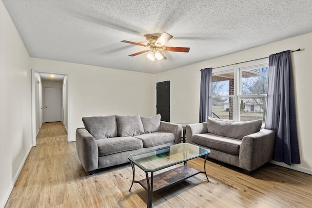 living room featuring ceiling fan, a textured ceiling, and light wood-type flooring