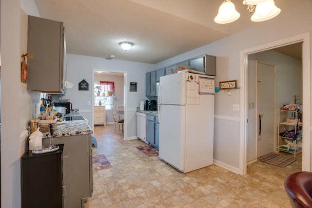 kitchen with a chandelier, a textured ceiling, gray cabinets, white appliances, and light stone countertops