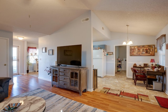 living room with lofted ceiling, a textured ceiling, light hardwood / wood-style floors, and a chandelier