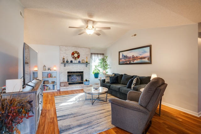 living room featuring lofted ceiling, a textured ceiling, ceiling fan, a fireplace, and hardwood / wood-style floors