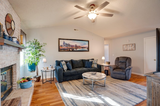 living room with lofted ceiling, ceiling fan, light hardwood / wood-style floors, brick wall, and a brick fireplace