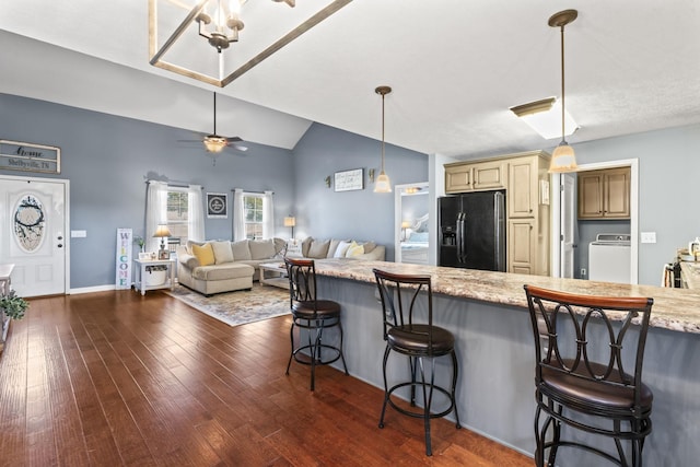 kitchen featuring black fridge with ice dispenser, washer / dryer, a breakfast bar area, light stone counters, and cream cabinets