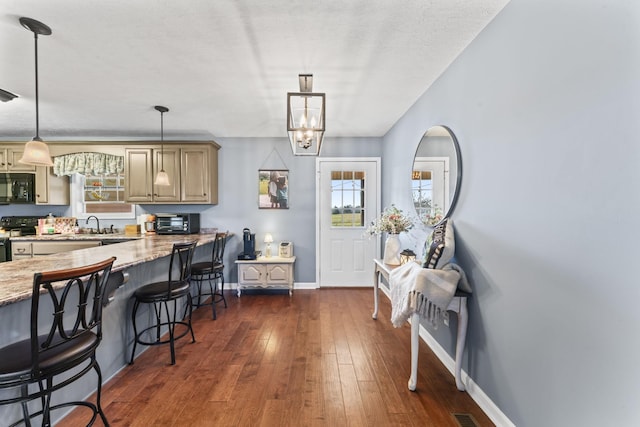 kitchen featuring a kitchen bar, dark hardwood / wood-style flooring, pendant lighting, light stone countertops, and black appliances