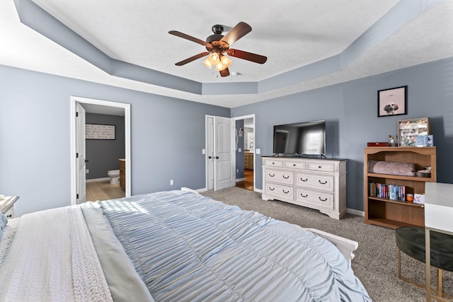 carpeted bedroom with a raised ceiling, ensuite bathroom, and ceiling fan