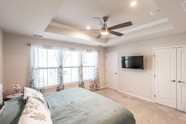 carpeted bedroom with a raised ceiling and ceiling fan