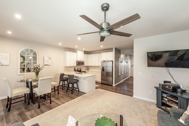 kitchen featuring dark wood-type flooring, a breakfast bar area, appliances with stainless steel finishes, white cabinets, and kitchen peninsula