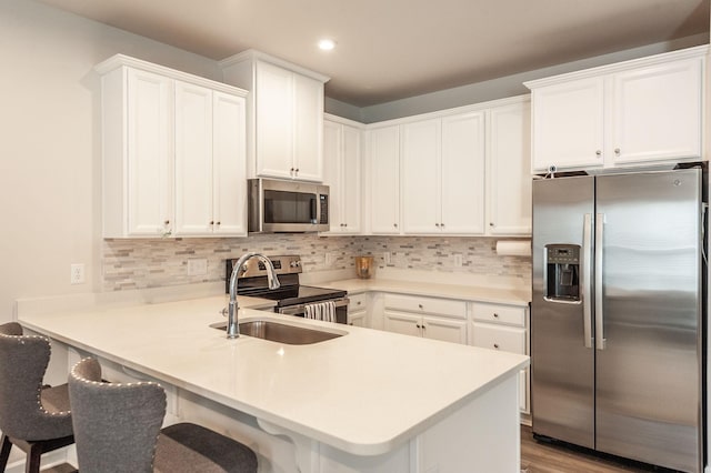 kitchen with sink, a breakfast bar, appliances with stainless steel finishes, white cabinetry, and kitchen peninsula