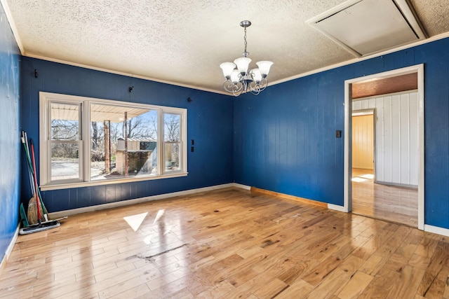 unfurnished room with crown molding, hardwood / wood-style floors, a textured ceiling, a chandelier, and baseboards