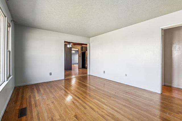 empty room with baseboards, visible vents, a textured ceiling, and light wood finished floors