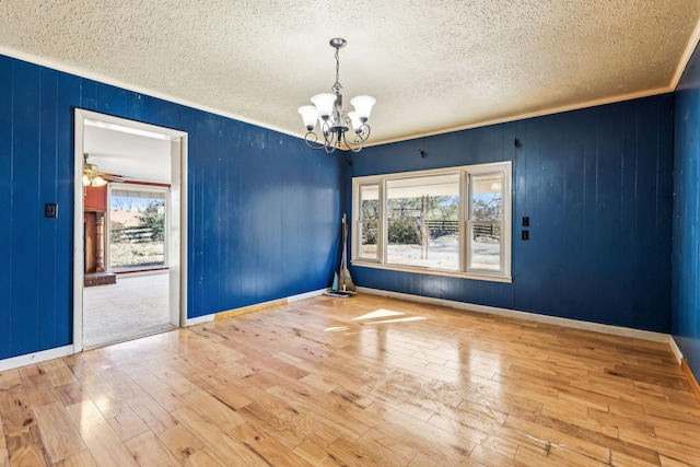 empty room with wood-type flooring, ornamental molding, a textured ceiling, a chandelier, and baseboards