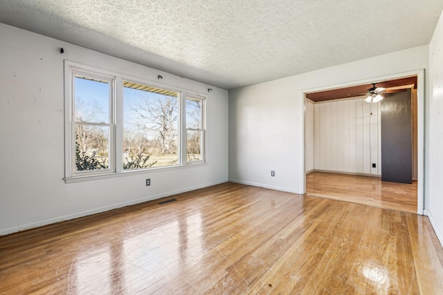 empty room with light wood finished floors, baseboards, visible vents, and a textured ceiling