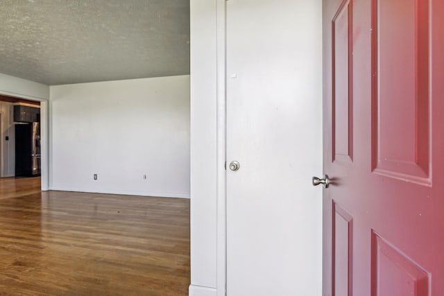 empty room featuring a textured ceiling, baseboards, and wood finished floors