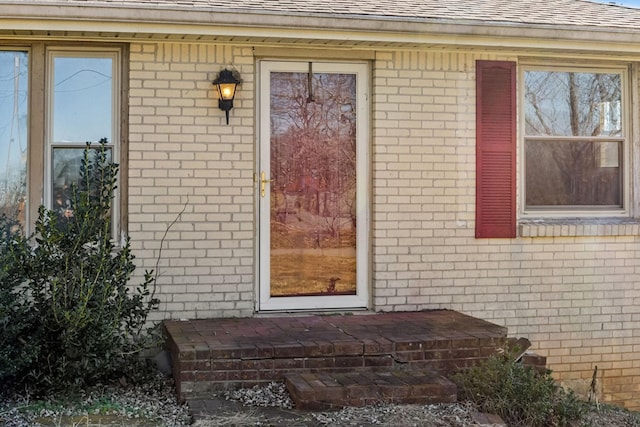 view of exterior entry featuring brick siding and roof with shingles