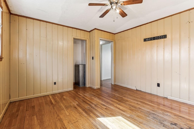 empty room with ornamental molding, a ceiling fan, baseboards, and wood finished floors