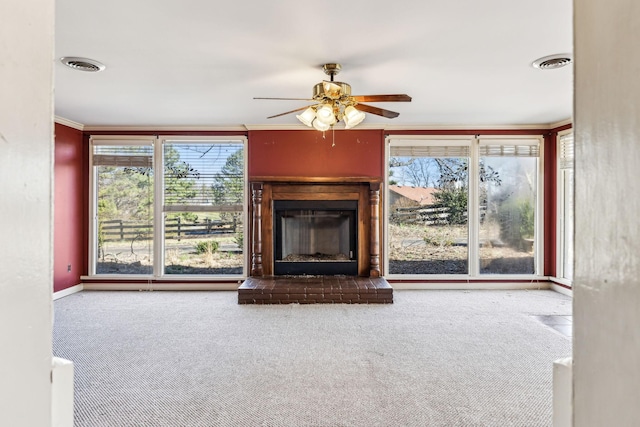 unfurnished living room with a fireplace with raised hearth, ornamental molding, visible vents, and a healthy amount of sunlight