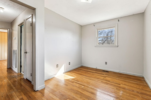 empty room featuring wood-type flooring, visible vents, baseboards, and a textured ceiling