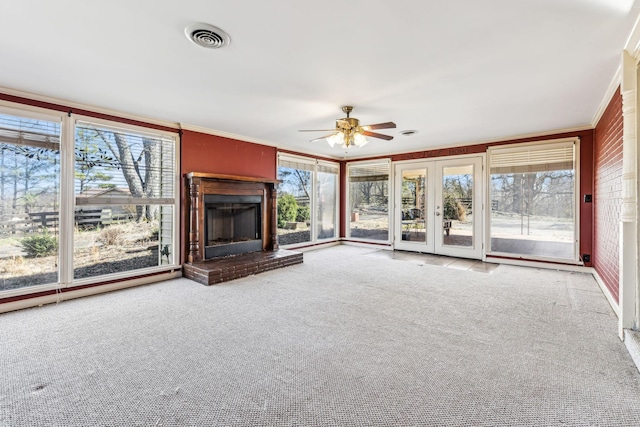 unfurnished living room featuring crown molding, a fireplace with raised hearth, visible vents, carpet flooring, and ceiling fan