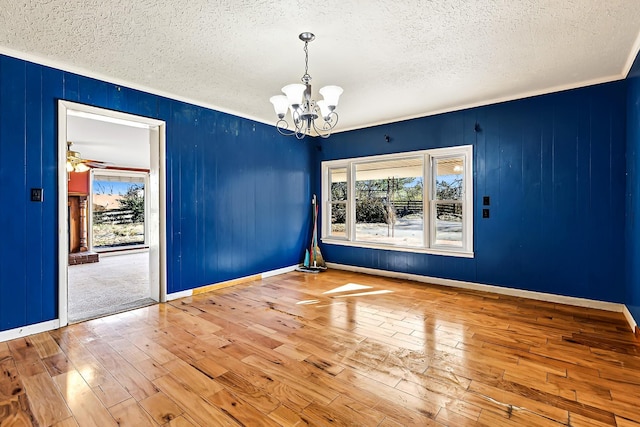 empty room with a textured ceiling, hardwood / wood-style floors, ceiling fan with notable chandelier, and baseboards